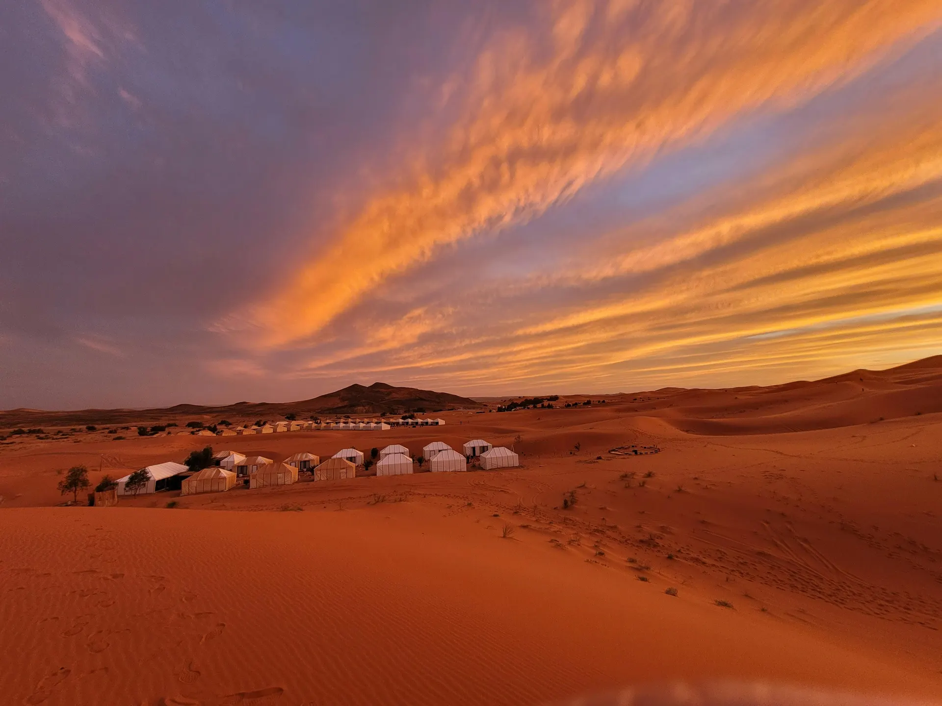 Premium desert camp and dunes at golden hour with adventurous tourism mood